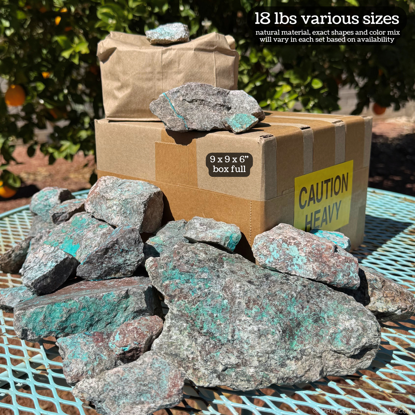 A cardboard box with a pile of various sizes of rough rock spread on and around it on a turquoise-colored table. The image is labeled 18 lbs various sizes, natural material, exact shapes and color mix will vary in each set based on availability. The cardboard box is labeled 9 by 9 by 6 inch box full, and has a "caution: heavy" sticker.