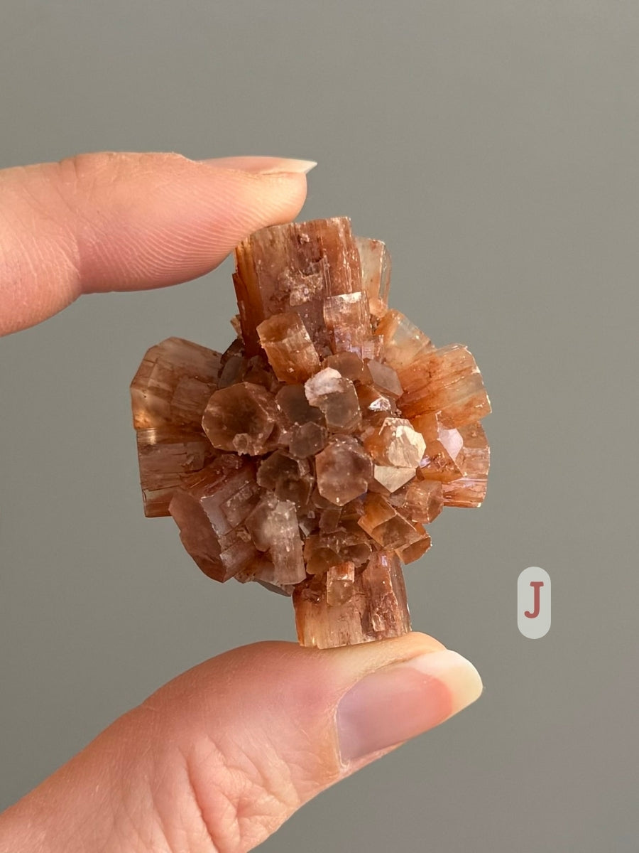 A piece of sputnik aragonite held between two fingers to show small scale. The aragonite is labeled as option J