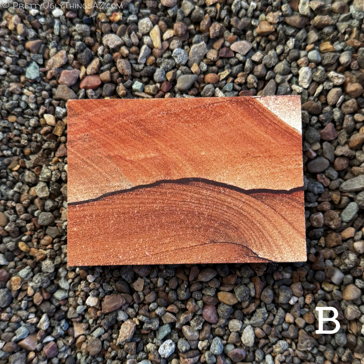Option B, a standard rectangle slab with saturated red-orange color. A curving dark iron band runs across the length, appearing like low hills under a brighter sky. The sandstone above the line is a lighter orange color with one corner white, layering running diagonally. Below the line, the sandstone is a less saturated brown, with curving layers.
