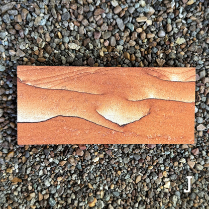 Option J, a long rectangular piece with simple pattern, that is mostly a red-orange color without layering. The color fades to near-white along one edge of several thin dark iron bands that snake across the surface.